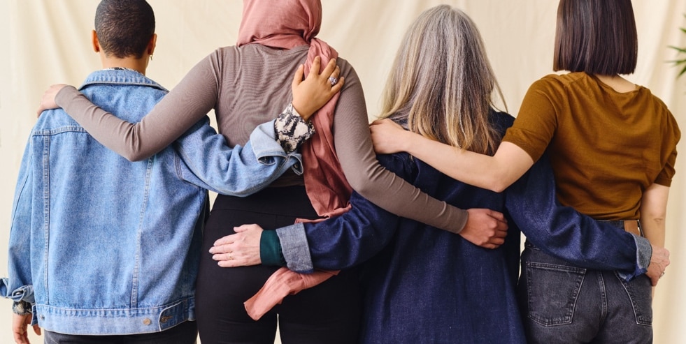 Four women standing arm in arm, photographed from behind
